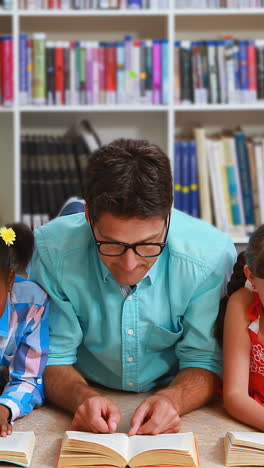 maestro y niños acostados en el suelo leyendo un libro en la biblioteca
