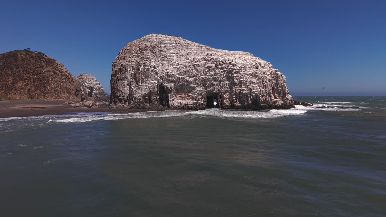 Dinamico primo piano con drone che rivela le intricate texture e le grotte marine dell'enorme roccia Piedra de la Iglesia nell'oceano