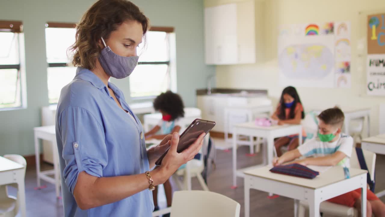 maestra que usa una máscara facial usando una tableta digital en la escuela