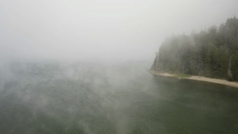 aerial view over misty water, passing the lakeshore and a beach at a lake, in usa