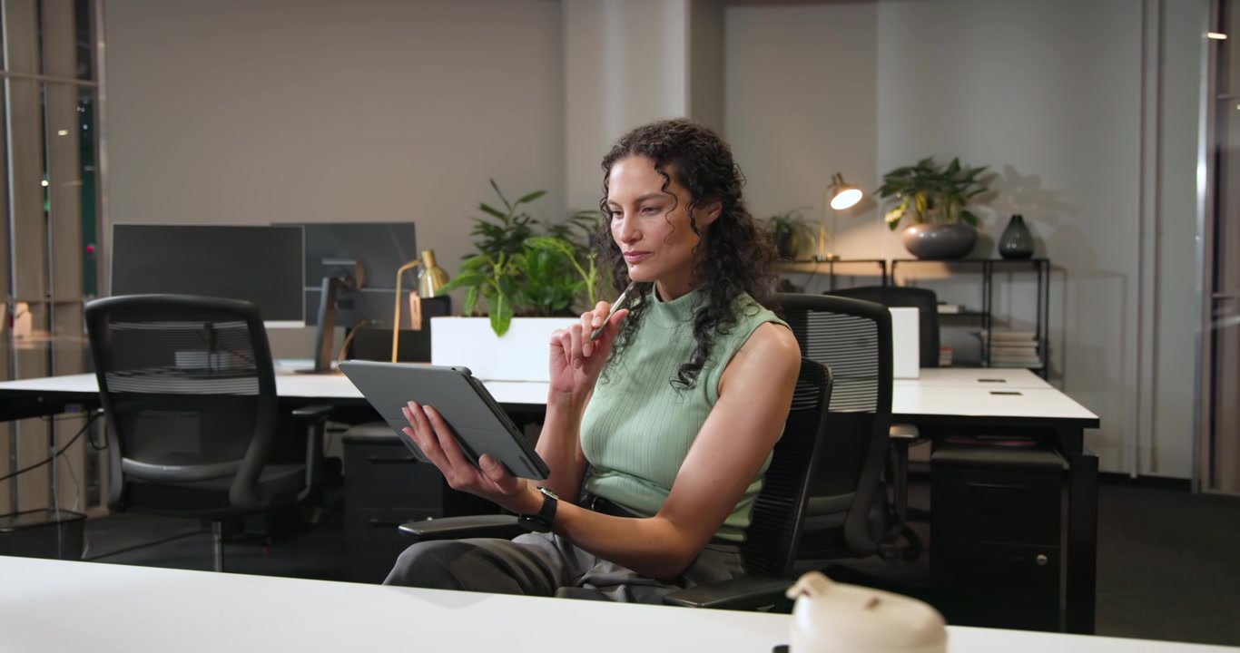 Donna seduta su una sedia che prende uno stilo, toccando e scorrendo su un tablet mentre esamina contenuti alla postazione di lavoro