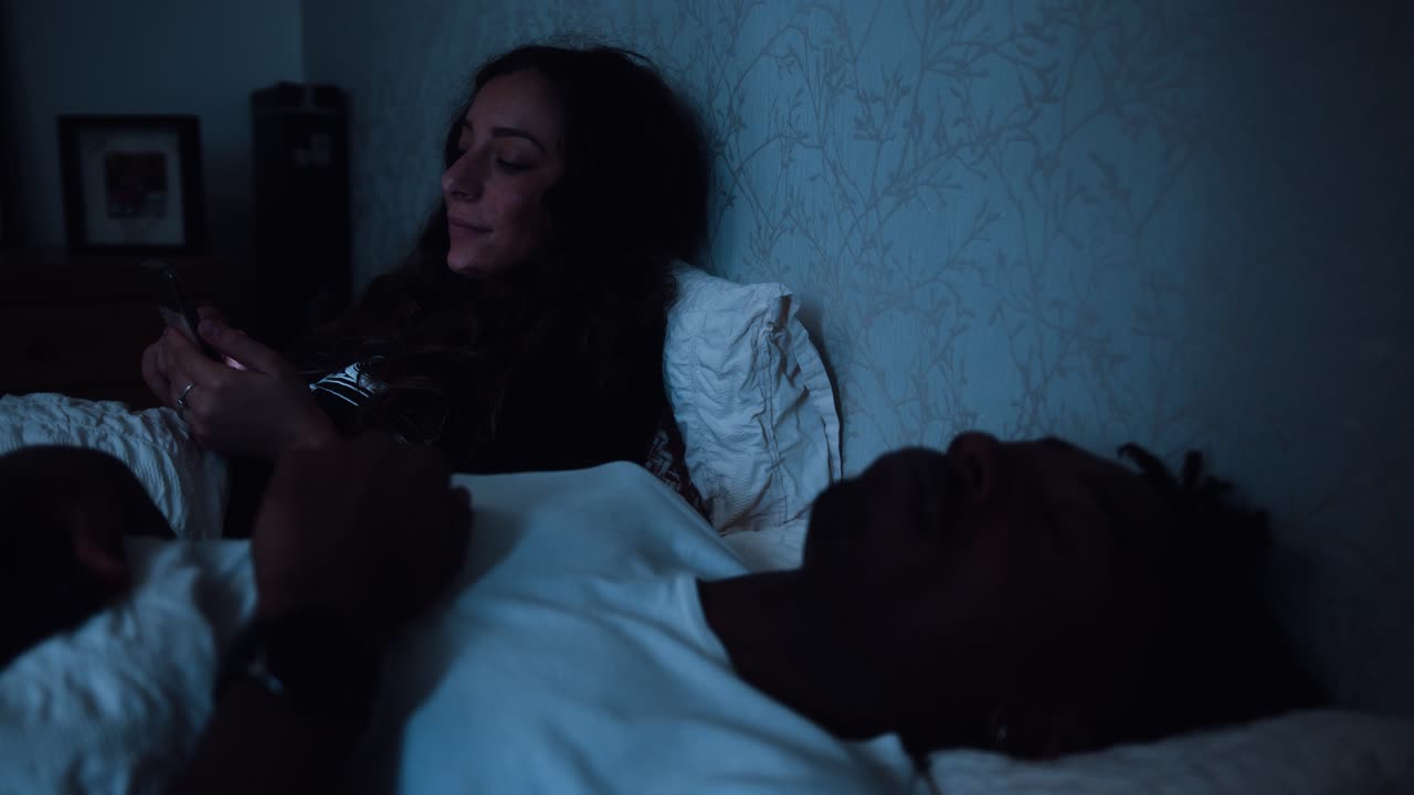 mujer joven se desplaza a través de su teléfono inteligente mientras está sentada en la cama por la noche