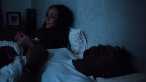 mujer joven se desplaza a través de su teléfono inteligente mientras está sentada en la cama por la noche