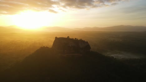 aerial drone shot over sigiriya lion rock in sri lanka at sunrise surrounded by dense green forest. sunlight shining over the rock