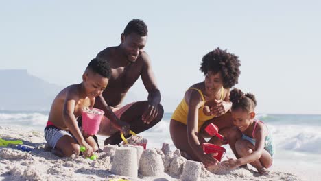 smiling african american family building sandcastle with american flag on sunny beach