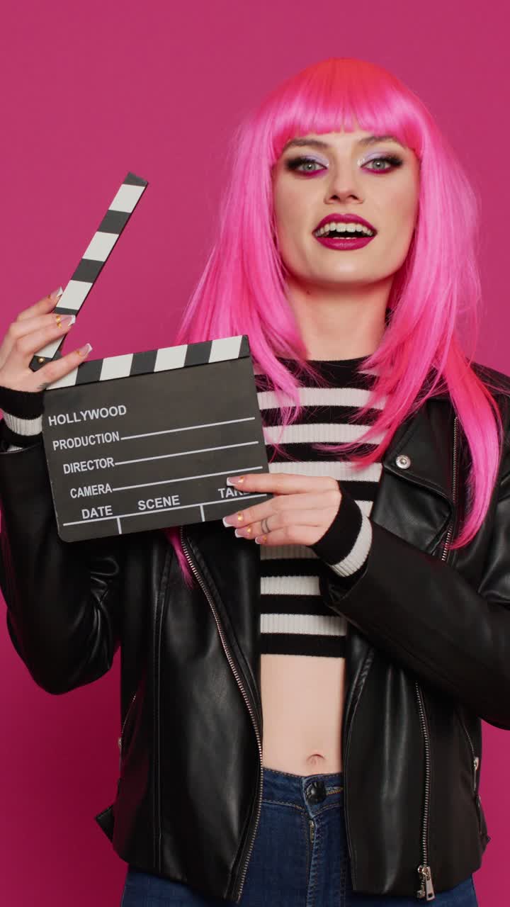 Vídeo vertical: alegre videógrafa sujetando una claqueta y diciendo «¡Acción!»
