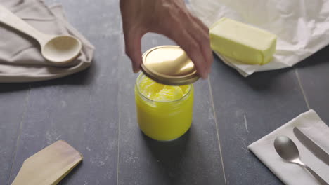 Man's-hand-takes-creamy-butter-ghee-from-a-pot-with-knife