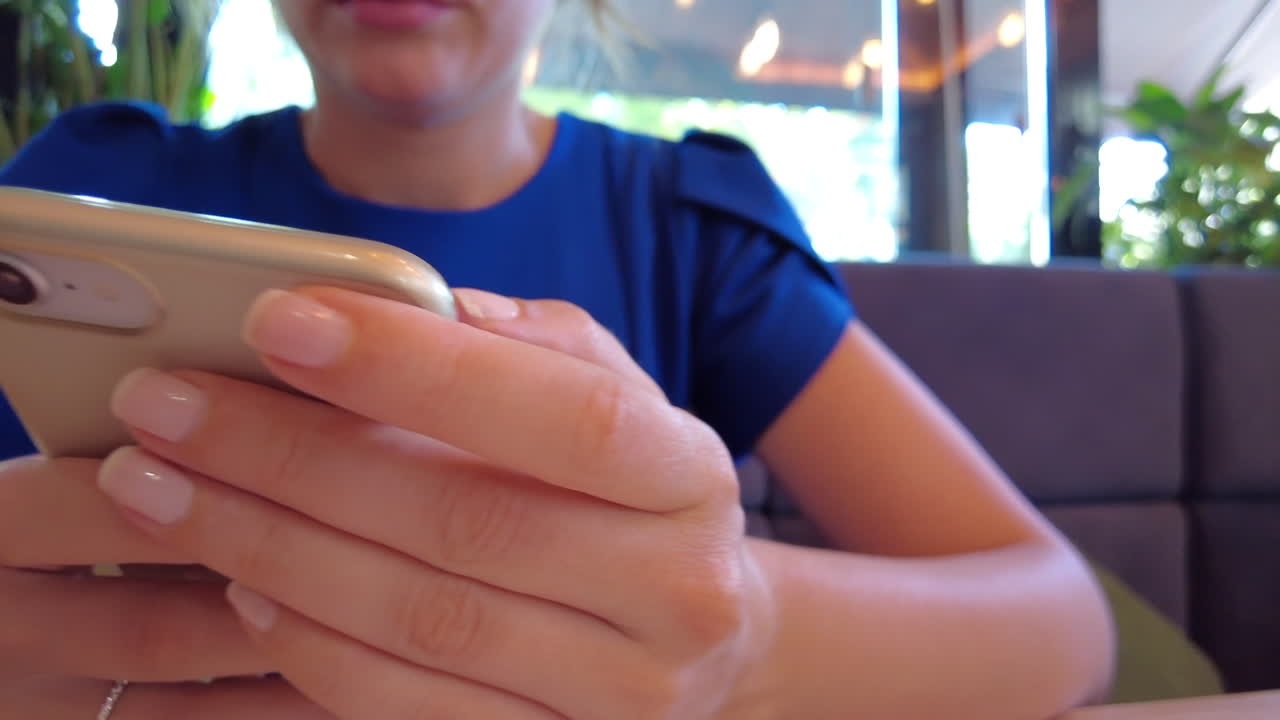 Donna con vestito blu che scorre contenuti sul telefono a un tavolo di un ristorante