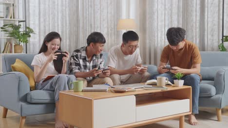 asian teen group playing game on smartphone, break time after working on online project, students with books and laptop studying at home