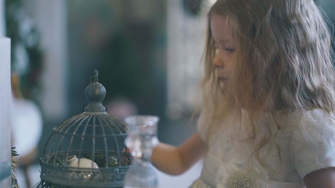 금발 소녀가 방에 있는 장식용 새장을 쳐다본다