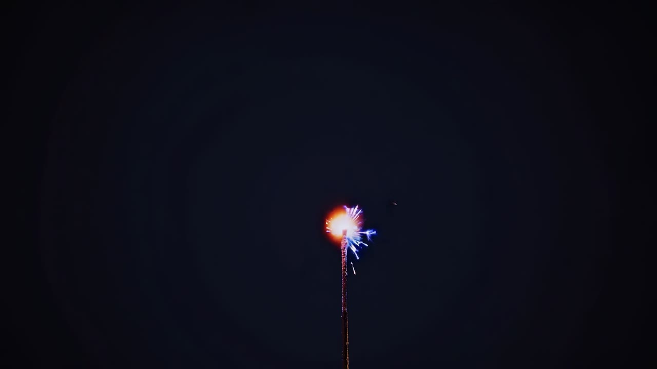 A low-angle video shot of a single sparkler against a dark sky, capturing its bright, dynamic sparks