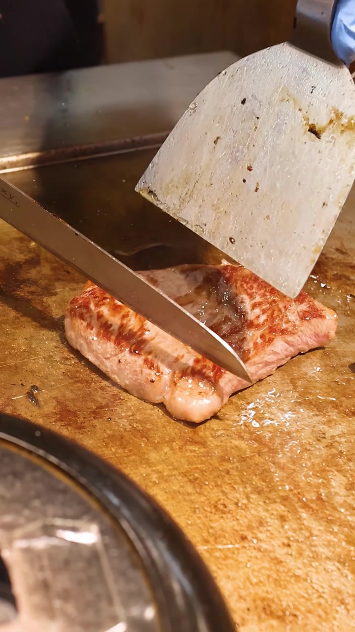 Lo chef usa una spatola e un coltello per affettare manzo wagyu marmorizzato su una piastra.