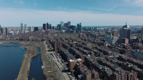 Aerial-ascending-footage-of-large-city.-Residential-neighbourhood-on-Charles-river-waterfront-and-downtown-high-rise-office-towers-in-distance.-Boston,-USA