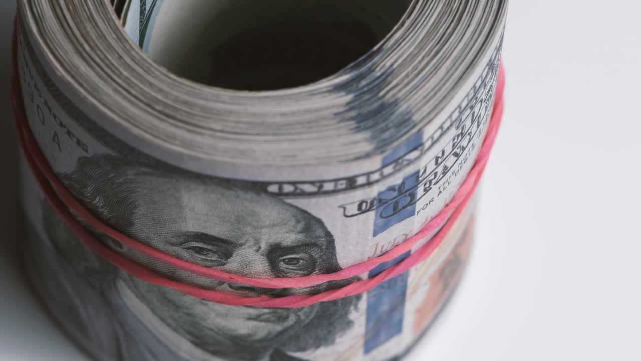 Nærbilde av en rull med hundre-dollarsedler holdt sammen med et gummibånd.