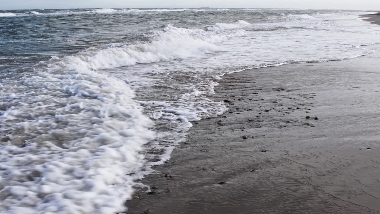 화창한 날에 모래 해변에 도달하는 넓은 바다의 파도의 낮은 각도 샷