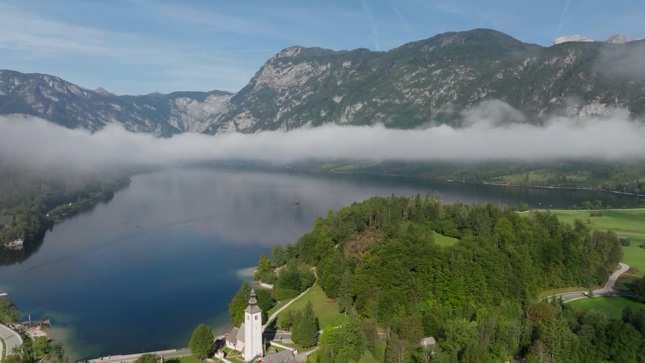Veduta aerea del Lago di Bohinj e della sua chiesa mentre nuvole basse entrano nella valle