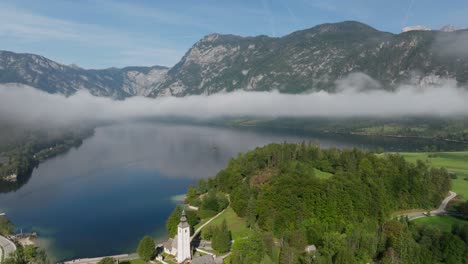 aerial view of lake bohinj and its church while low clouds are entering the valley