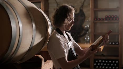 adult man winemaker at winery checking glass looking quality while standing between the barrels in the cellar controlling wine making process - real people traditional and industry wine making concept