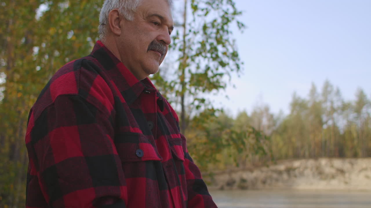 pescador de mediana edad está pescando solo por la caña girando carrete de pie en la orilla del río en el bosque en el día de otoño