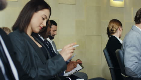 다민족 기업인들이 회의실 의자에 앉아 듣는 동안 공책에 글을 쓰는 모습을 자세히