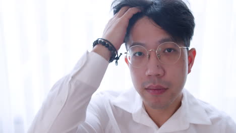 Close-up-Asian-man-with-glasses-and-healthy-good-hair-looking-to-the-camera-and-spoiling-himself-by-tidying-his-hair