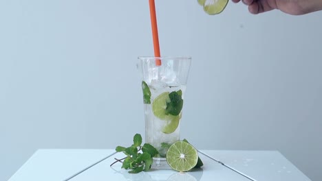 man takes out straw and lime slice from glass on white table