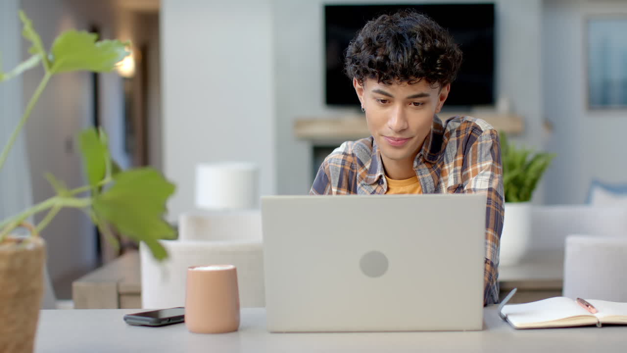 Using laptop and studying, young man working at home with notebook nearby