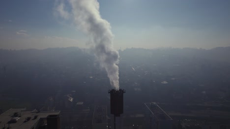 humo saliendo de una chimenea con una ciudad contaminada al fondo