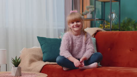 Retrato-De-Una-Niña-Adorable-Sentada-Sola-En-Un-Sofá-En-Casa-Mirando-La-Cámara-Y-Sonriendo