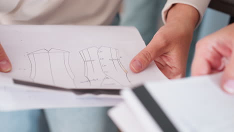 closeup view of student sketching clothing design outlines on white sheet of paper while teacher hands over writing pen during creative learning session teamwork fashion project planning