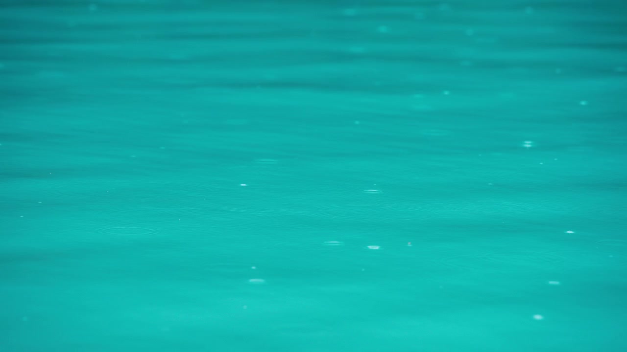 Pioggia che cade sulla superficie dell'acqua blu.