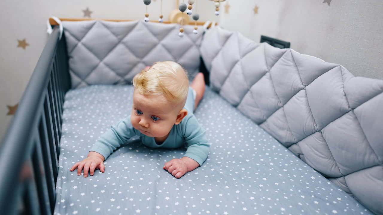Lovely cute child lying on the belly in the blue crib. Cot mobile is hanging above the baby boy.