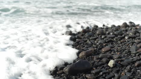 calm wave rolls in on black glistening pebble beach, tenerife