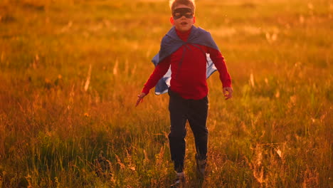 Ein-Junge-In-Einem-Anzug-Und-Einer-Superheldenmaske-Mit-Rotem-Umhang-Läuft-Bei-Sonnenuntergang-über-Das-Feld-Auf-Dem-Gras-Und-Träumt-Und-Stellt-Sich-Vor,-Er-Sei-Ein-Held.