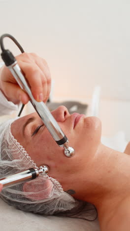 la doctora esteticista hace a la mujer micro corrientes terapia facial usando impulsos eléctricos en el salón de spa