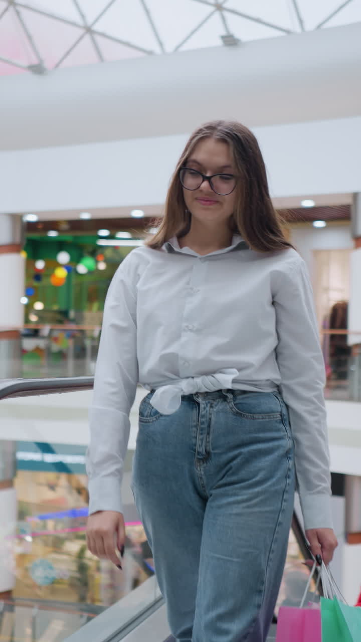 joven baja de la escalera mecánica ascendente con confianza con bolsas de compras, otras personas visibles detrás de ella en un ambiente vibrante y moderno del centro comercial