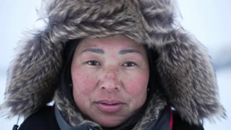 a woman with a fur-lined hood stands against a snowy backdrop. her expression reflects strength and determination in the harsh winter environment.