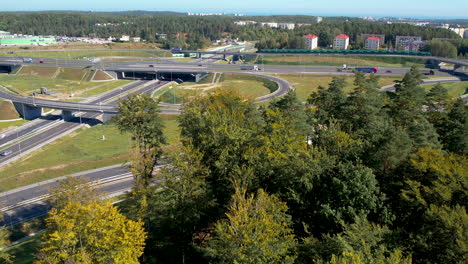 Aerial-over-the-woods-of-a-busy-highway-intersection-near-Wielki-Kack,-Gdynia,-Poland,-in-sunny-weather-and-the-Baltic-Sea-in-the-horizon