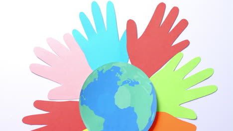 close-up van handen samen met een globe gemaakt van kleurrijk papier op een witte achtergrond met kopieerruimte