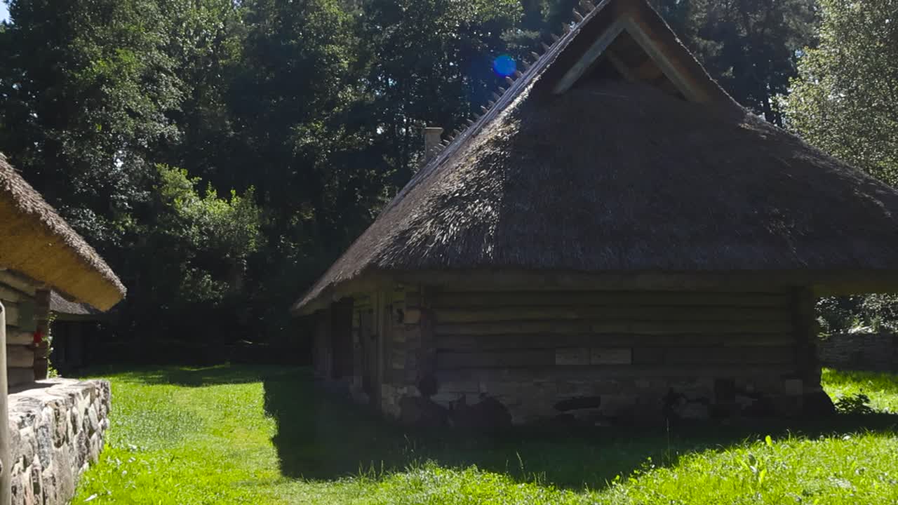 Gorgeous old and traditional log buildings with thatched roof in the middle of a countryside sunny forest during summer day. Grassy green garden around them, sun rays and lense flare visible