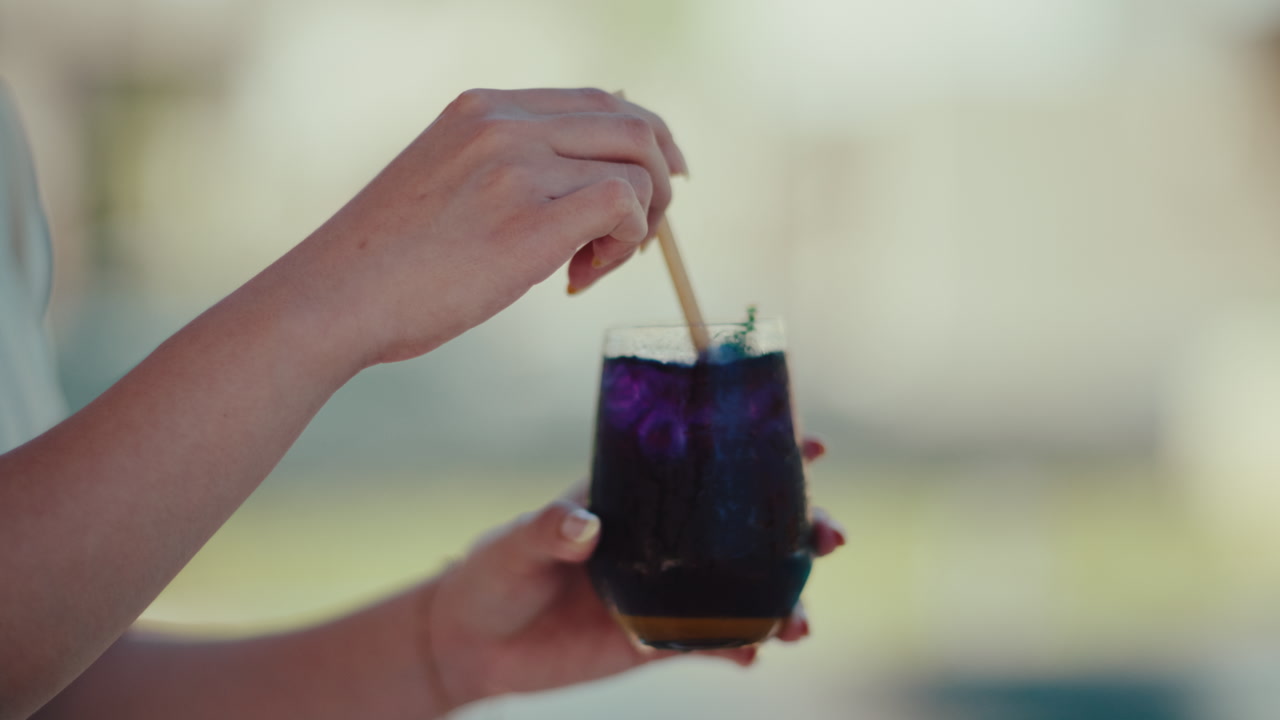 Woman's hand stirring a refreshing blue butterfly pea tea drink with a straw