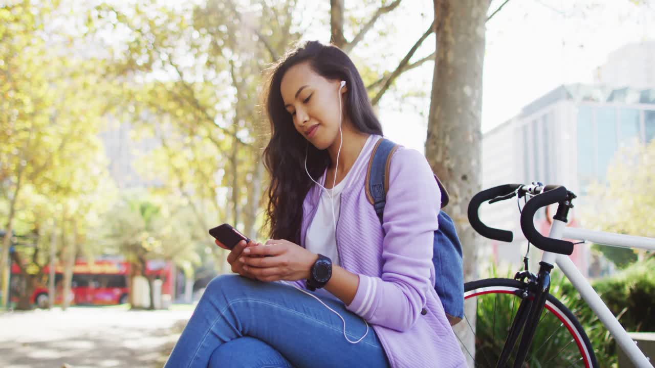 mujer asiática con auriculares usando un teléfono inteligente sentada en el parque