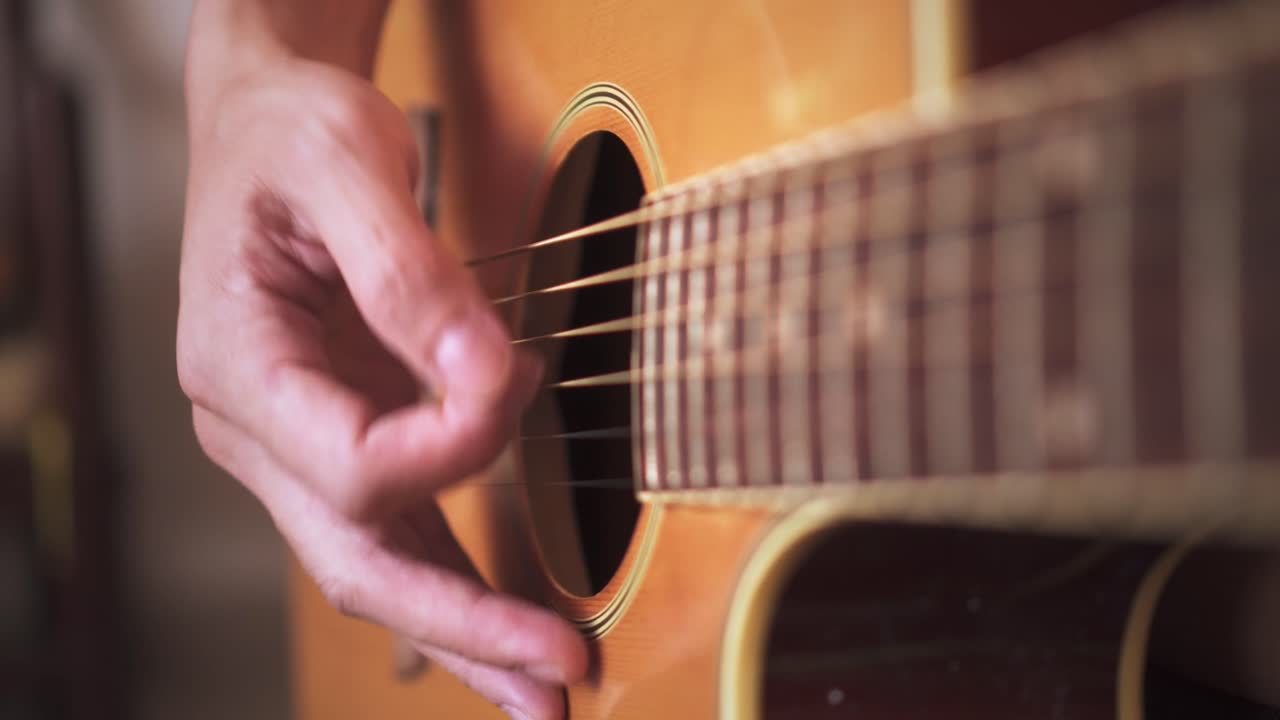 primer plano de las yemas de los dedos de la mano rasgueando patrones hacia arriba y hacia abajo en la guitarra acústica