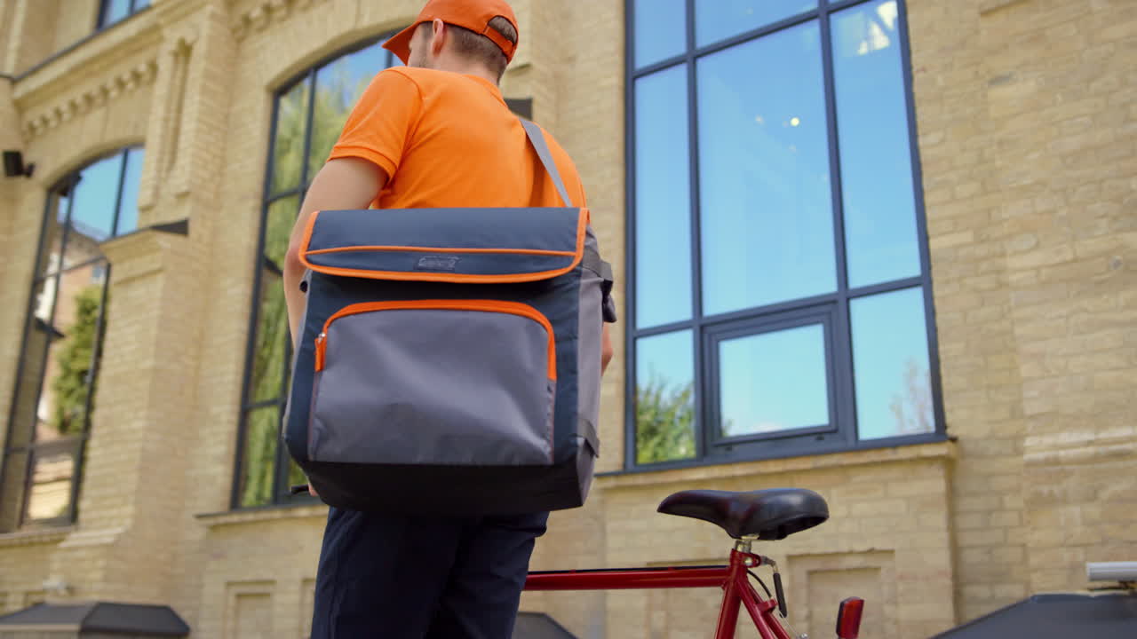 Man delivering food with bike in downtown. Courier looking for address outdoors.