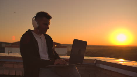 rear view of a man in headphones listening to music and working on the roof of a building at sunset with a view of the city from a height. roof of a skyscraper at sunset.