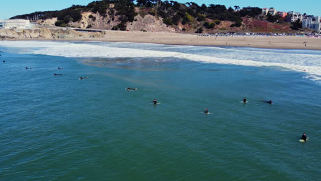 Surfers-Lying-and-Sitting-On-Surfboard-Floating-In-The-Sea-At-Ocean-Beach-With-Cliff-House-In-San-Francisco,-California