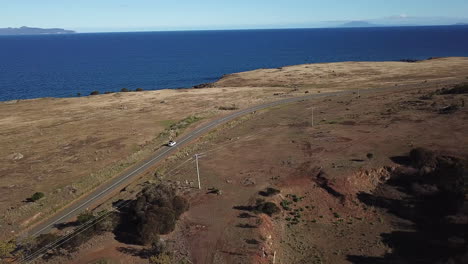 drone pan alrededor de coche solitario conduciendo a lo largo de la carretera costera con árboles y océano azul, tasmania australia