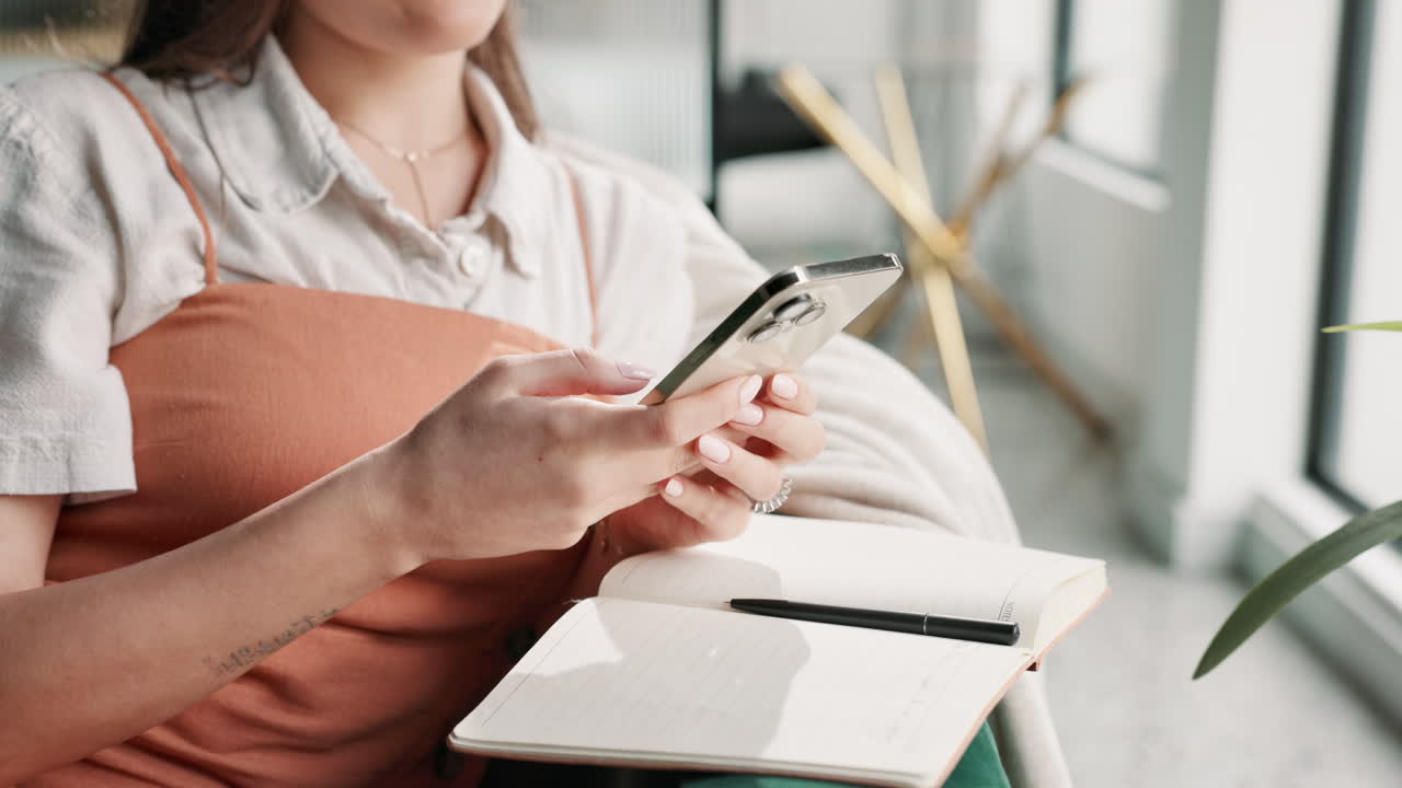 A woman using her phone and notebook indoors