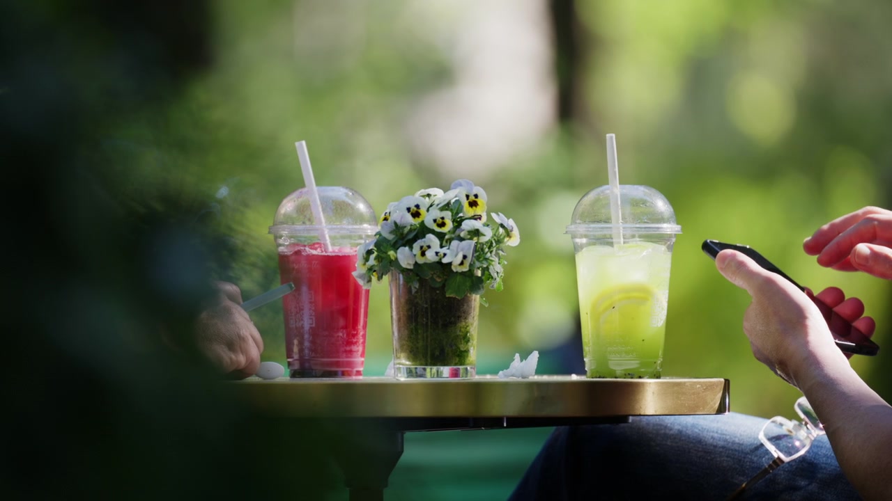 Brightly colored cold beverages displayed on an outdoor cafe table with decorative flowers and soft focus greenery in the background