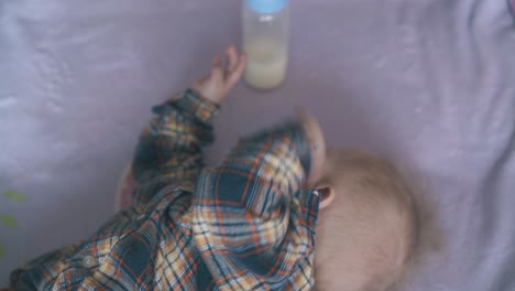el bebé gracioso come una mezcla de leche fresca en una cama suave con cuadros rosados